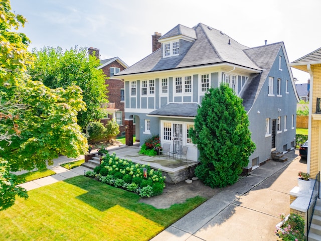 view of front of home with a patio area, a chimney, a front yard, and stucco siding