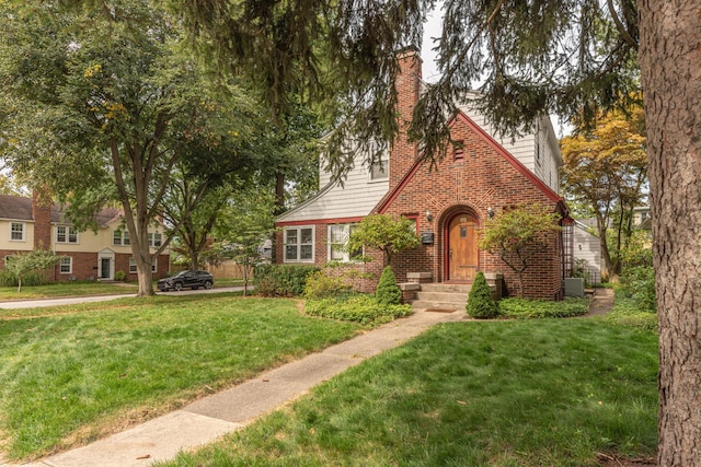 tudor-style house featuring brick siding, a chimney, and a front yard