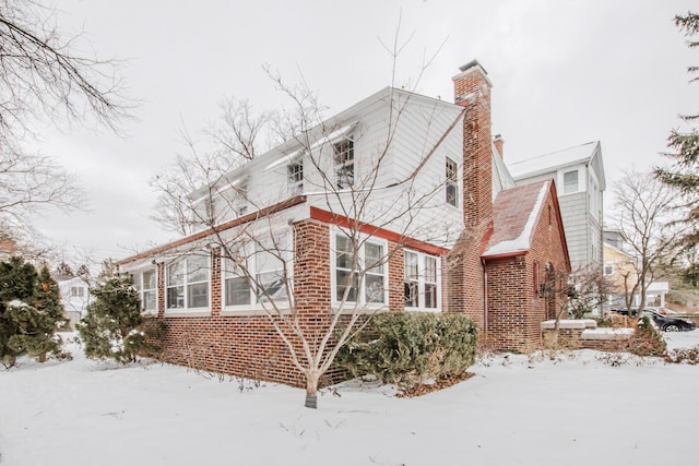 view of snow covered exterior featuring brick siding and a chimney