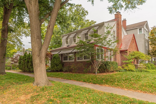 view of front of home featuring brick siding, a front lawn, and a chimney