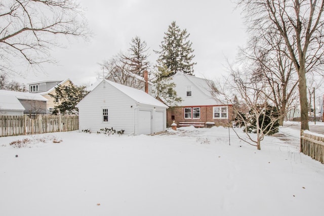 snow covered property featuring an outbuilding, brick siding, and fence