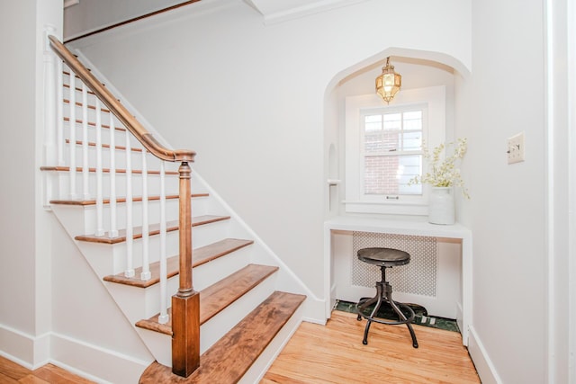 staircase with arched walkways, wood finished floors, and baseboards