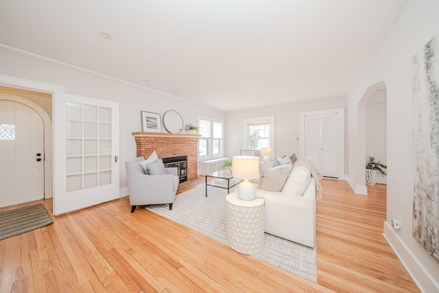 living room with arched walkways, crown molding, a fireplace, wood finished floors, and baseboards