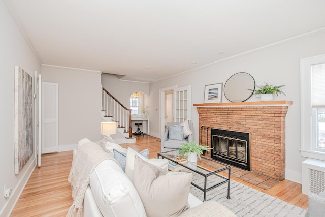 living area featuring baseboards, light wood-style flooring, stairs, crown molding, and a fireplace