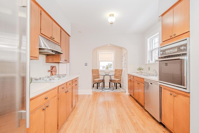 kitchen featuring arched walkways, light wood-style floors, appliances with stainless steel finishes, light countertops, and under cabinet range hood