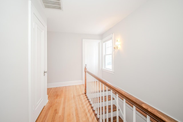 corridor featuring visible vents, baseboards, light wood finished floors, and an upstairs landing