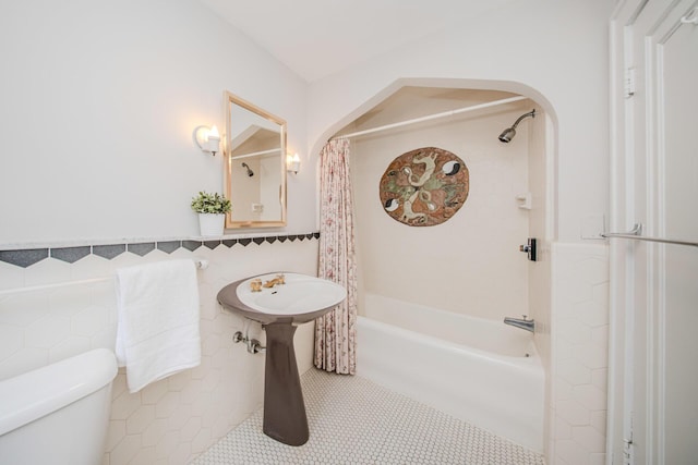 bathroom featuring tile patterned flooring, toilet, tile walls, wainscoting, and shower / bath combo