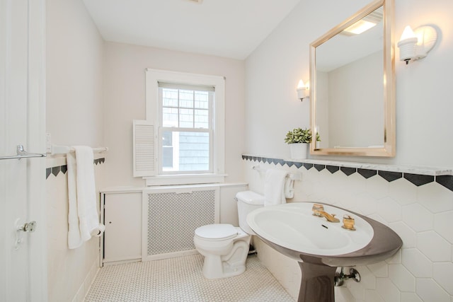 bathroom with tile patterned flooring, toilet, tile walls, wainscoting, and radiator