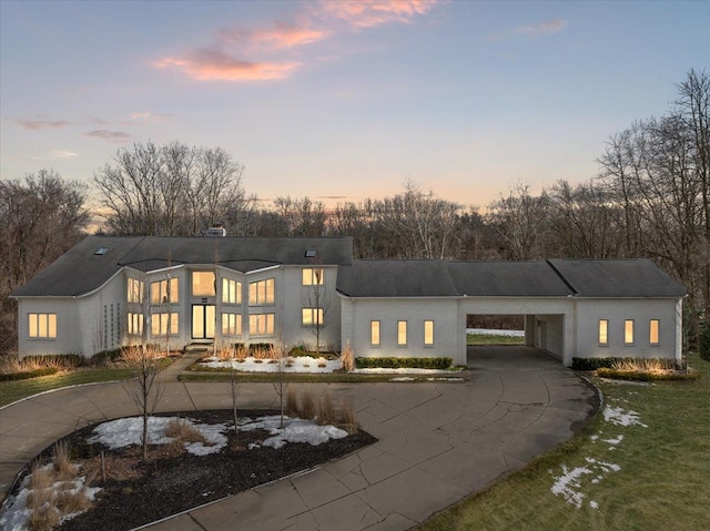 back of property at dusk with a carport and curved driveway