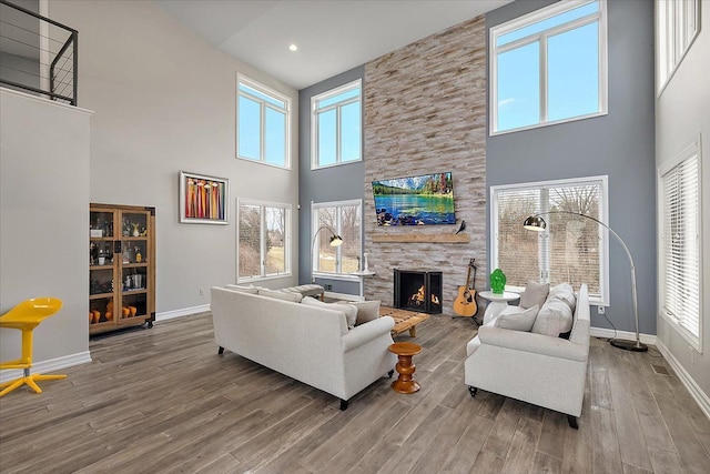 living area featuring wood finished floors, recessed lighting, a stone fireplace, baseboards, and a towering ceiling