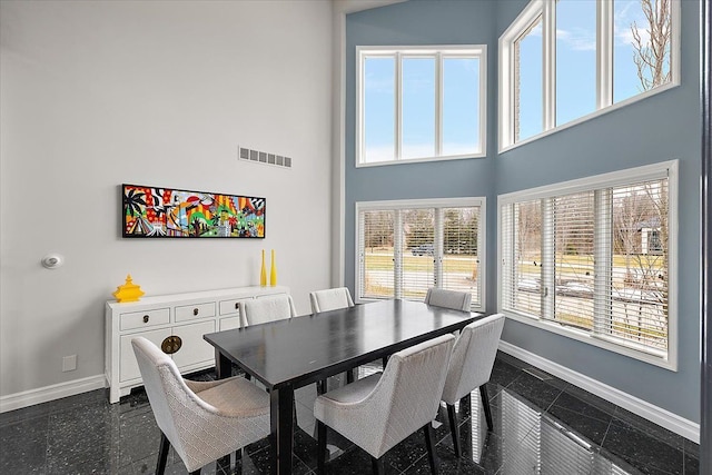 dining area featuring granite finish floor, visible vents, baseboards, and a towering ceiling