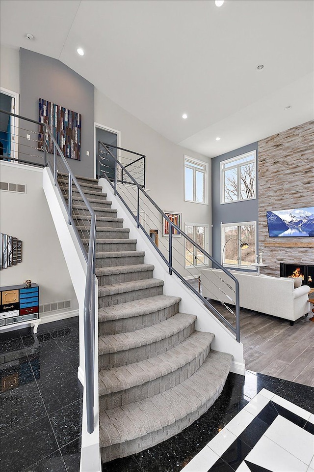 stairs featuring visible vents, recessed lighting, high vaulted ceiling, and a lit fireplace