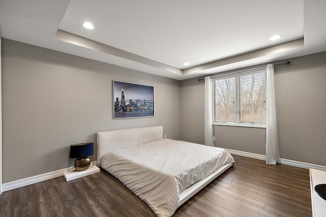 bedroom featuring recessed lighting, a tray ceiling, baseboards, and wood finished floors