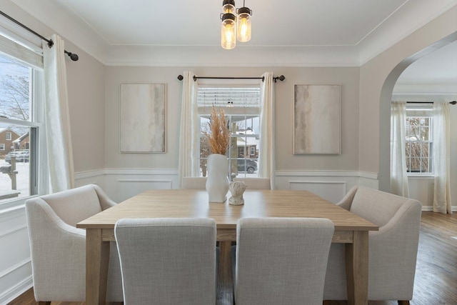 dining space with arched walkways, a wealth of natural light, and wainscoting