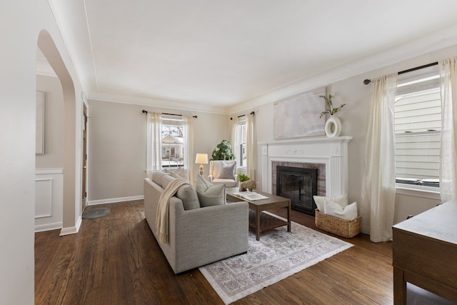 living room with dark wood-style floors, arched walkways, crown molding, a brick fireplace, and baseboards