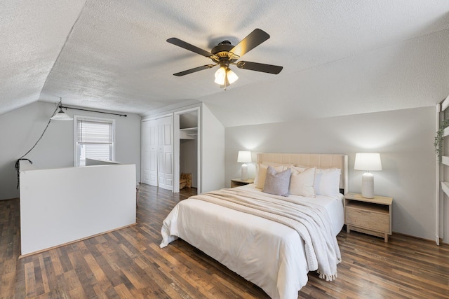 bedroom with a closet, dark wood-type flooring, vaulted ceiling, a textured ceiling, and ceiling fan