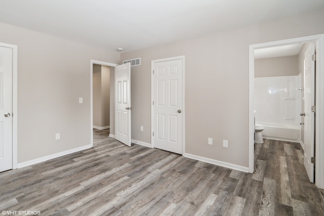 unfurnished bedroom with baseboards, connected bathroom, visible vents, and wood finished floors