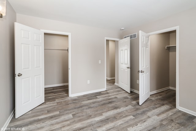 unfurnished bedroom featuring light wood-style flooring, visible vents, a walk in closet, and a closet