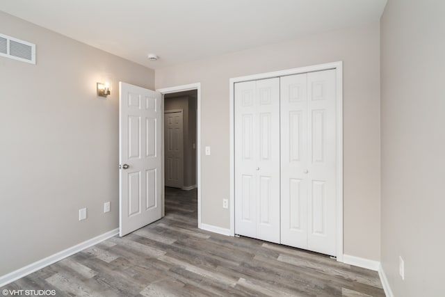 unfurnished bedroom featuring baseboards, a closet, visible vents, and wood finished floors