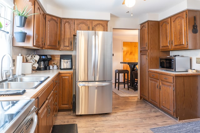 kitchen with brown cabinetry, appliances with stainless steel finishes, light countertops, light wood-style floors, and a sink