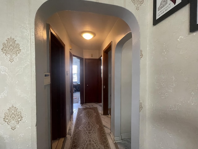 hall featuring marble finish floor, arched walkways, and a textured wall