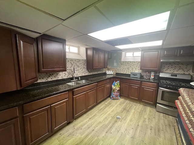 kitchen featuring backsplash, light wood-style floors, stainless steel gas stove, a sink, and dark stone countertops