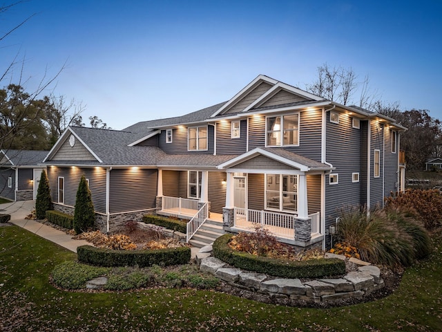 craftsman inspired home featuring a porch, a front yard, stone siding, and roof with shingles