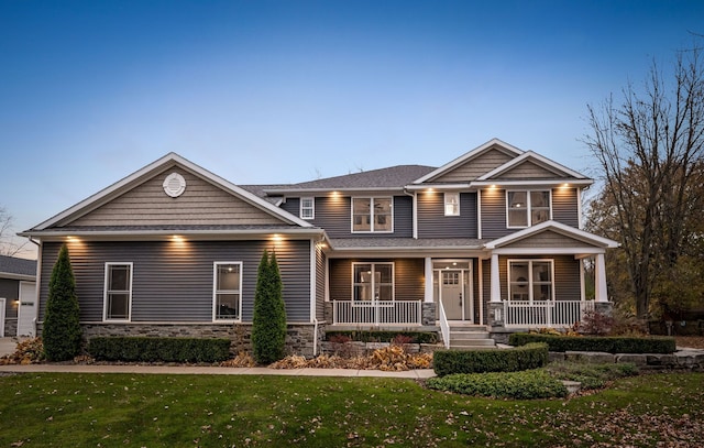 craftsman-style house with stone siding, a porch, and a lawn