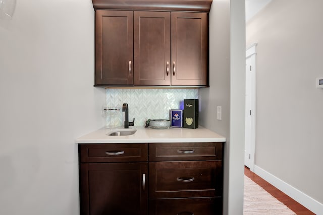 bar featuring tasteful backsplash, light wood-style floors, a sink, and baseboards