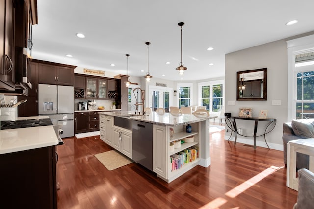 kitchen with dark brown cabinetry, an island with sink, glass insert cabinets, refrigerator with ice dispenser, and stainless steel dishwasher