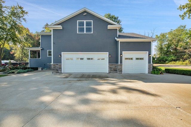 view of side of home featuring driveway, stone siding, and an attached garage