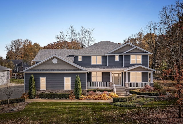 view of front of property with stone siding, a shingled roof, a front lawn, and covered porch