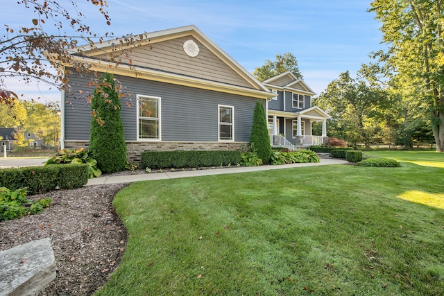 craftsman-style house featuring stone siding, covered porch, and a front lawn