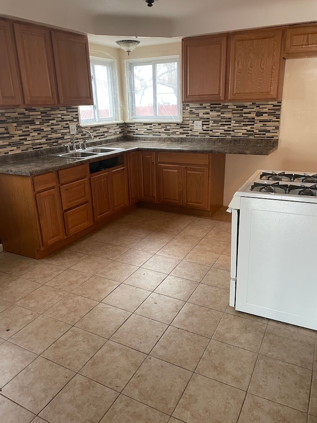 kitchen with dark countertops, backsplash, brown cabinetry, white range with gas cooktop, and a sink