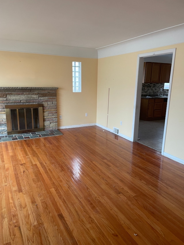 unfurnished living room with baseboards, visible vents, wood finished floors, and a stone fireplace