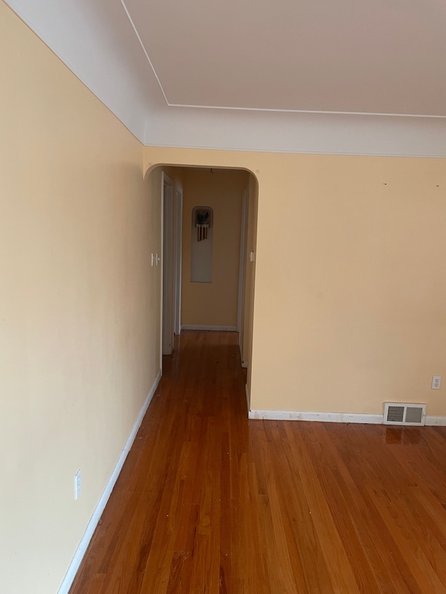 hall with baseboards, visible vents, arched walkways, and wood finished floors