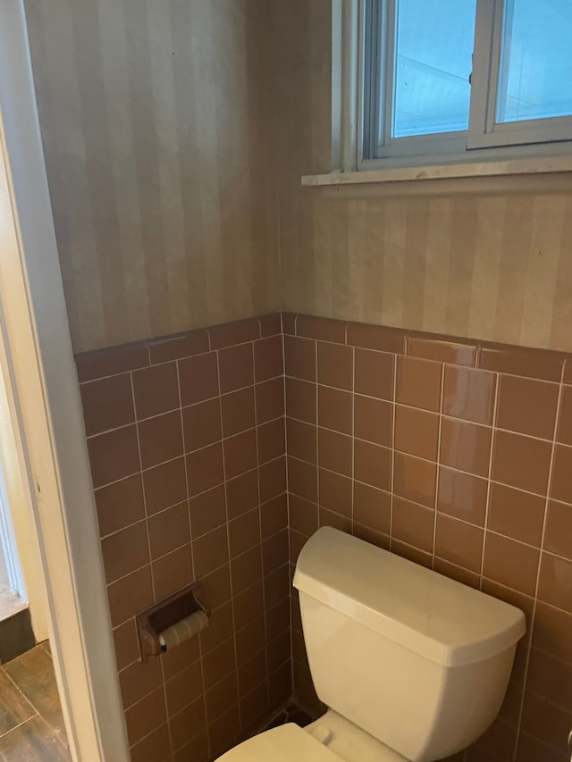 bathroom with toilet, a wainscoted wall, wallpapered walls, and tile walls