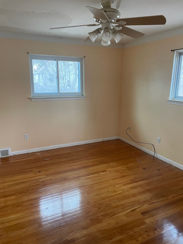 empty room featuring a ceiling fan, light wood-type flooring, visible vents, and baseboards