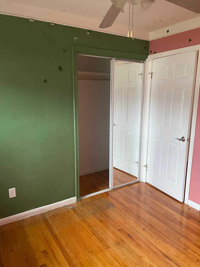 unfurnished bedroom featuring a closet, ceiling fan, baseboards, and wood finished floors