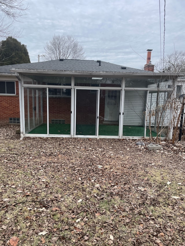 rear view of house featuring brick siding, a sunroom, roof with shingles, crawl space, and a chimney