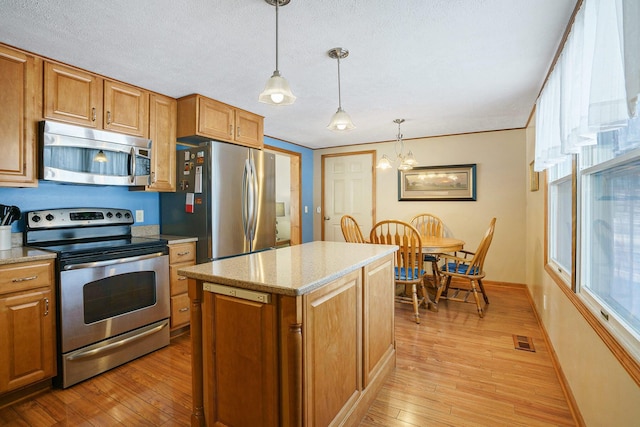 kitchen featuring a center island, visible vents, hanging light fixtures, appliances with stainless steel finishes, and brown cabinetry