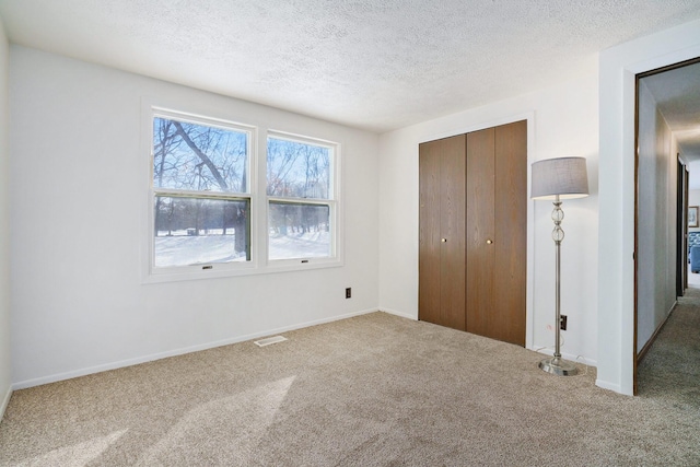 unfurnished bedroom with baseboards, visible vents, a textured ceiling, carpet floors, and a closet