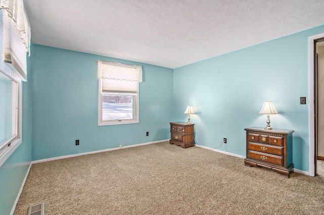 unfurnished room with a textured ceiling, carpet flooring, visible vents, and baseboards