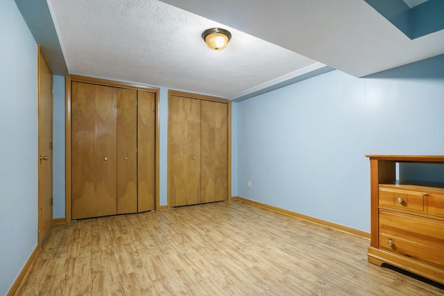 unfurnished bedroom with light wood-type flooring, a textured ceiling, baseboards, and two closets