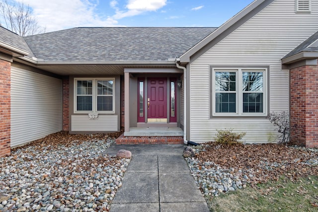 doorway to property with a shingled roof and brick siding