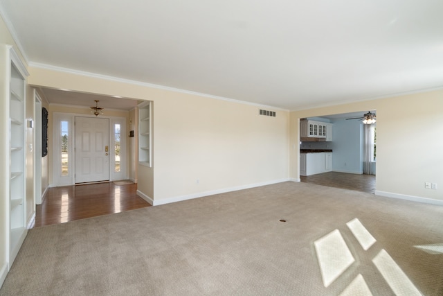 unfurnished living room featuring carpet floors, baseboards, visible vents, and ornamental molding