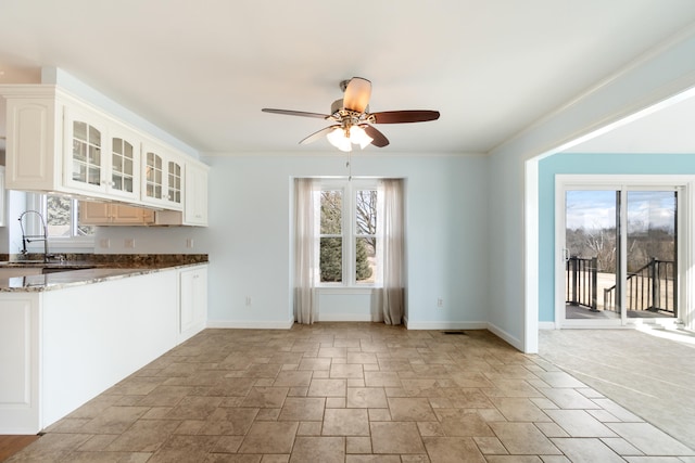 kitchen featuring dark stone counters, ornamental molding, glass insert cabinets, and baseboards