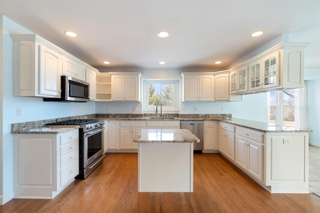 kitchen featuring light stone counters, stainless steel appliances, a peninsula, a sink, and light wood-type flooring