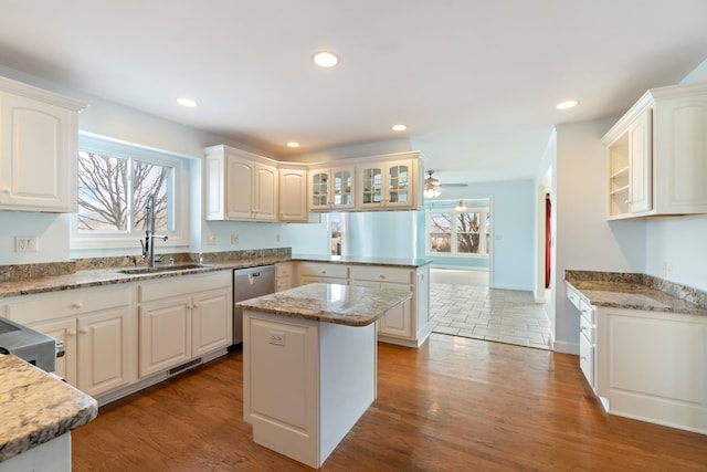 kitchen with wood finished floors, a peninsula, stainless steel dishwasher, and a sink