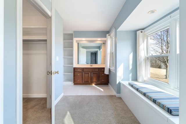 bathroom featuring carpet floors, a walk in closet, vanity, and baseboards